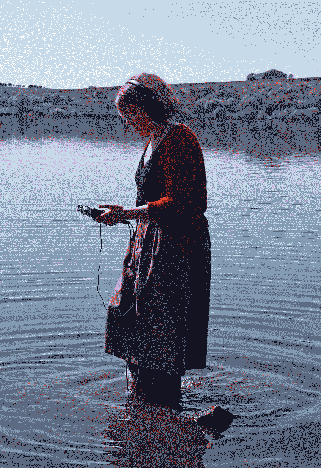 Sophie Cooper stood in a lake using field recording equipment.